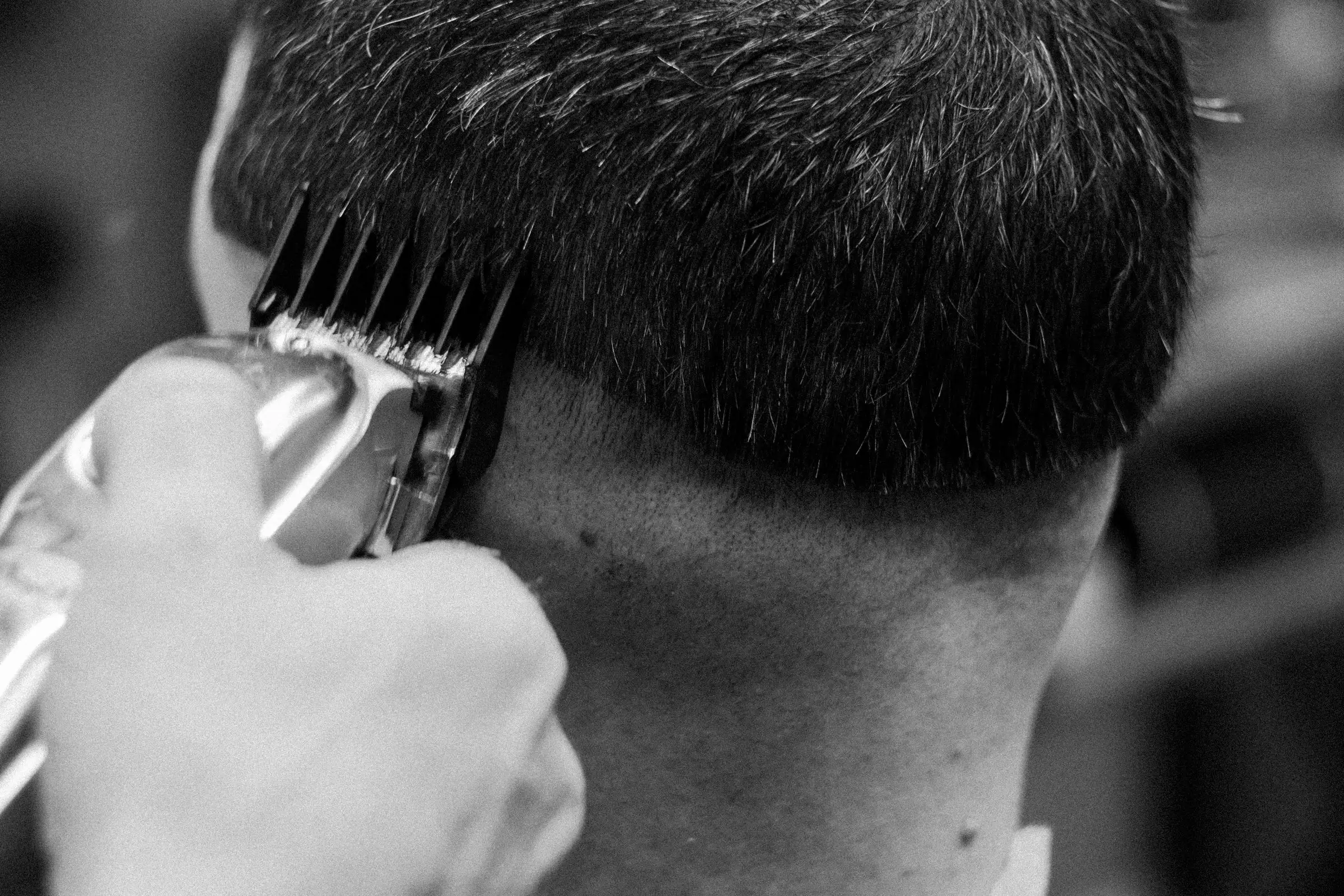 Black-and-white close-up of a barber fading a haircut with clippers.