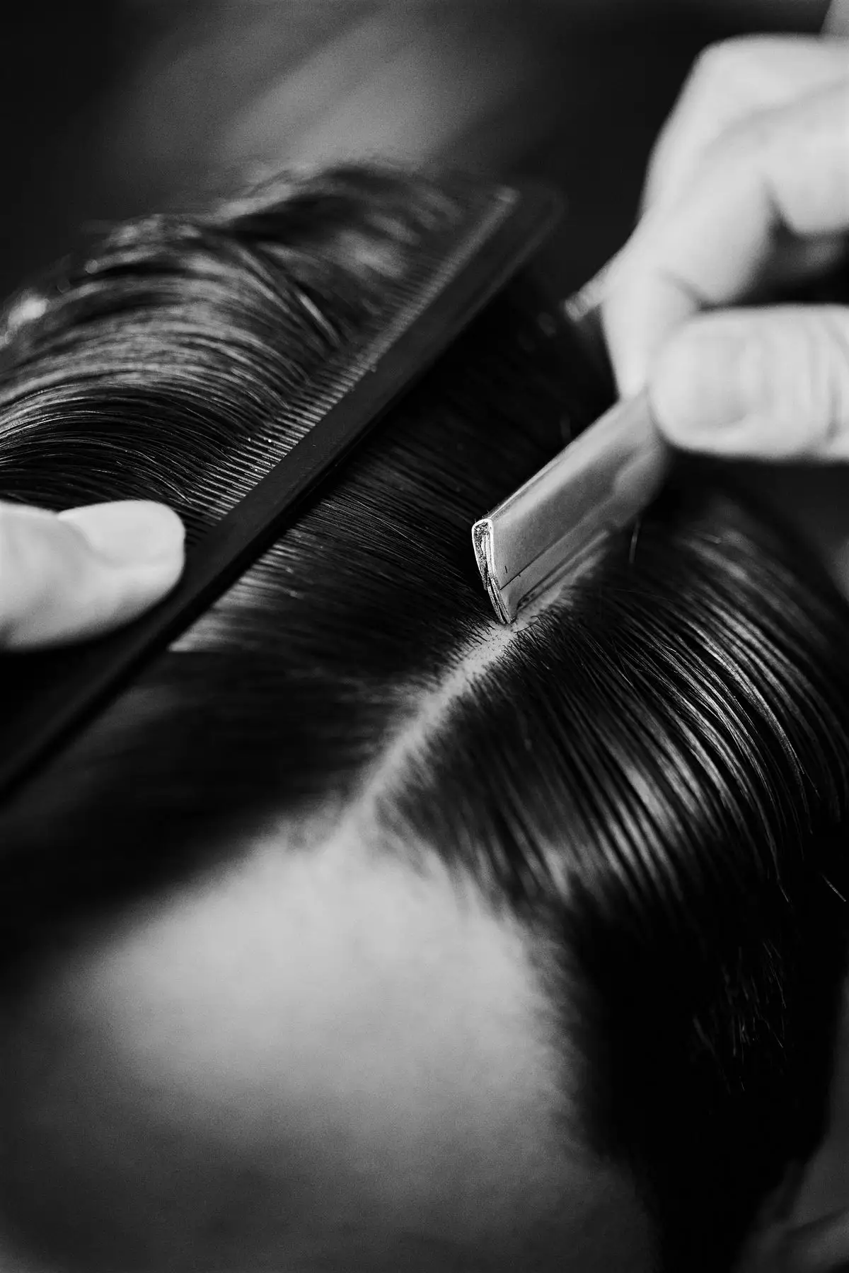A barber styling hair with a comb and razor, in black and white.