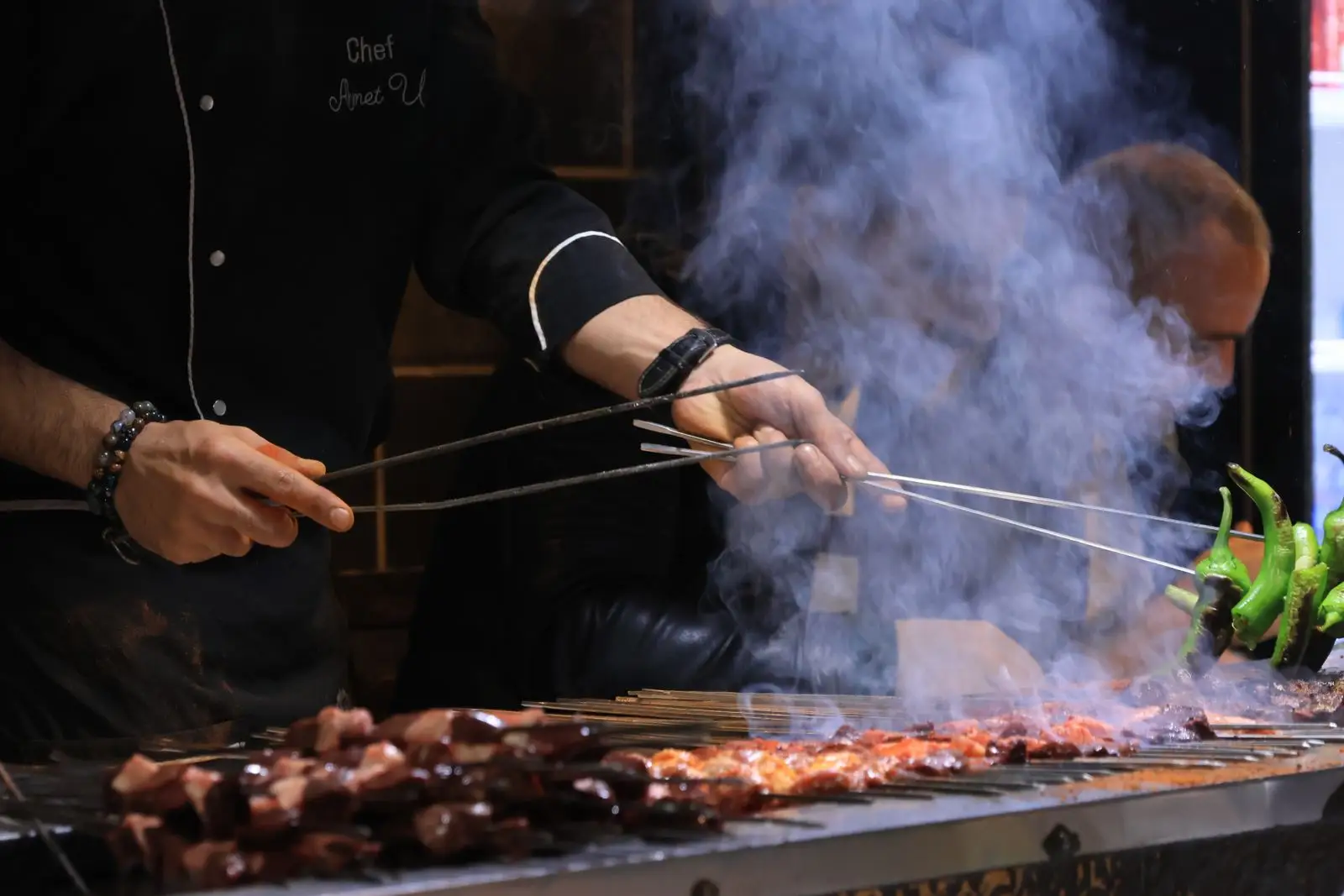 A cook grilling skewers over open flame.